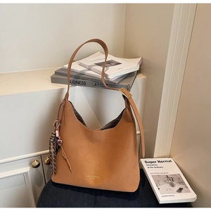 Macro detail of caramel hobo bag featuring woven tassel charm and golden fashion logo