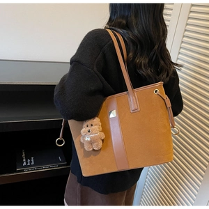 Detailed close-up of brown suede and leather tote bag with a cute teddy bear charm