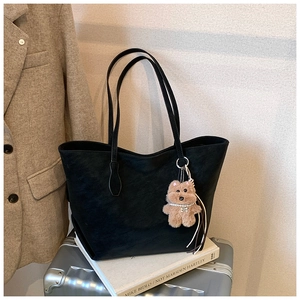 Detail of black tote bag with plush bear charm resting on luggage for travel