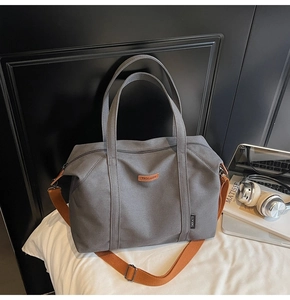 Detail of grey canvas travel tote bag with adjustable orange strap on white bedding