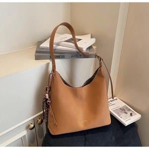 Close-up of caramel leather shoulder bag detail with plaid charm and gold text