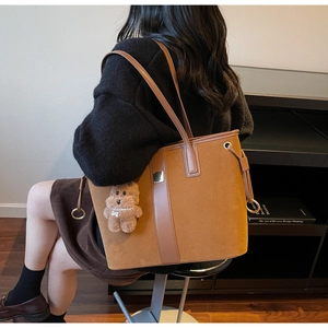 Detail of large brown suede tote bag with leather strap and plush bear charm on a model