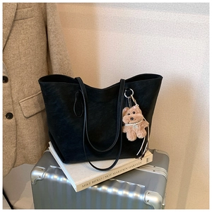 Detail of a black leather tote bag with a cute plush bear pendant on a silver suitcase