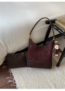 Dettaglio di un set borsa a secchiello vintage in pelle scamosciata bordeaux con orsetto