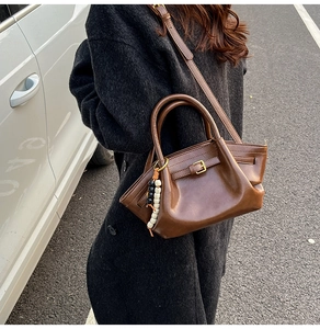 Detail of a dark brown crossbody bag featuring a beaded charm and draped leather texture