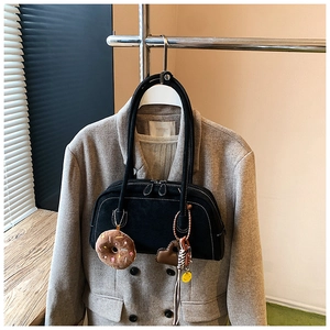 Detail of black suede shoulder bag with white contrast stitching and plush donut charm