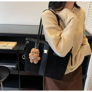 Detail of black suede tote bag featuring a decorative brown plush bear and golden ring charm