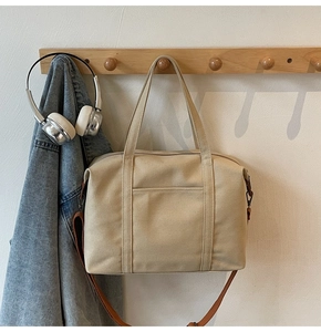 Close-up of beige canvas tote bag with brown leather strap hanging on a wooden hook