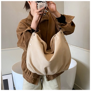 Detail of beige canvas hobo tote with brown leather strap and metal rivet accents