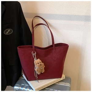 Macro detail of burgundy faux leather tote bag with a cute brown plush bear charm