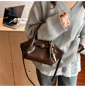 Dark brown leather tote bag with decorative buckle and beaded charm on office desk