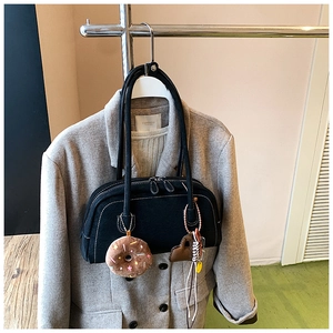 Close-up of black leather vintage Boston bag with plush donut charm on a grey wool coat