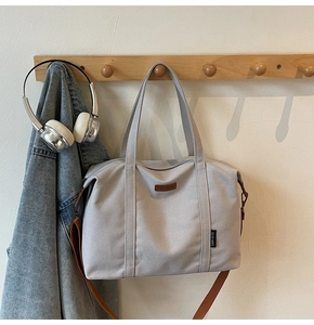 Detail of grey canvas tote bag with adjustable brown strap and logo patch on wooden hanger