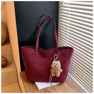 Detail view of burgundy leather tote bag with plush bear charm and sleek matte finish