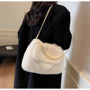 Gros plan du sac en peluche beige avec chaîne dorée porté sur un manteau noir