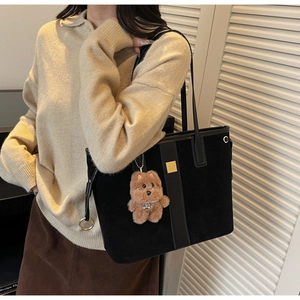 Detail of black suede tote bag with golden hardware and plush bear charm for autumn