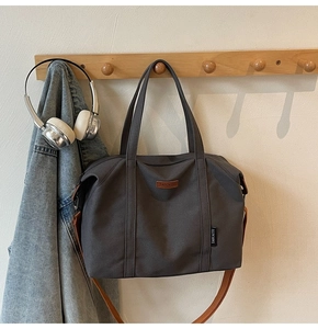 Detail of grey canvas tote bag with brown leather logo patch and adjustable strap