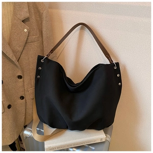 Detail of black canvas tote bag with silver rivets and brown faux leather handle