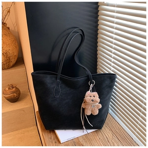 Detail of black tote bag with matte texture and a brown plush teddy bear charm
