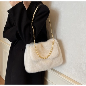 Gros plan d'un sac bandoulière en peluche blanche avec bandoulière chaîne dorée sur manteau