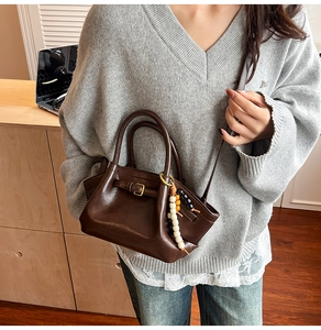 Close-up of a dark brown tote bag with decorative metal buckle and colorful beaded charm