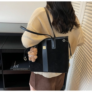 Detail of black suede tote bag with golden buckle and cute plush bear charm accessory