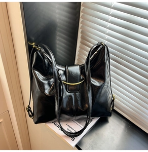 Close-up of black glossy leather tote bag with gold semi-circle hardware and top zipper