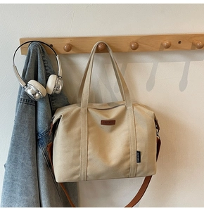 Detail of beige canvas tote with brown strap and leather logo on a wooden hanger