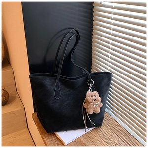 Detail of a large black matte leather tote bag featuring a cute brown plush bear charm