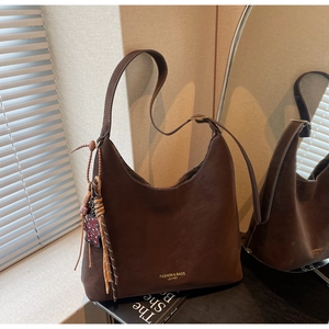 Detail of dark brown faux suede bucket bag with white contrast stitching and tassel charm