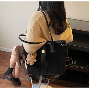 Detail of black matte tote bag with brown plush bear charm in a stylish commute setting