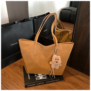 Caramel leather tote bag detail with cute plush bear charm on a stack of books