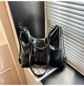 Close-up of black glossy oil wax leather shoulder bag with golden crescent metal buckle