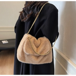 Détail du sac à bandoulière en peluche camel avec chaîne dorée porté sur un manteau noir