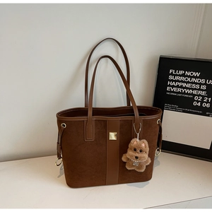 Close-up of brown suede tote bag with golden metal decor and a cute plush bear charm