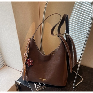 Detail of coffee brown leather tote bag with a red leopard print bear charm and gold text