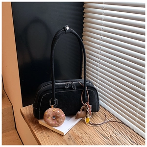 Detail of black suede shoulder bag with contrast stitching and colorful bag charms