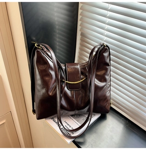 Close-up of deep brown oil-wax leather tote bag with gold metal bar detail on a windowsill