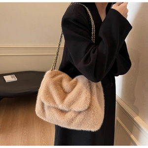 Détail d'un sac bandoulière en fausse fourrure beige avec chaîne dorée porté par un modèle