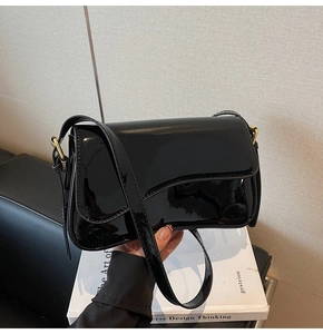 Close-up of black patent leather crossbody bag with a polished gold adjustable buckle