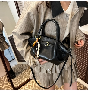 Detail view of black leather handbag featuring a chic wooden bead pendant and gold buckle