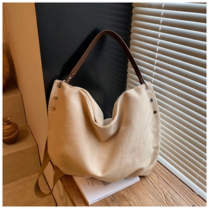 Detail of beige canvas tote bag with metal rivets and premium brown leather handle