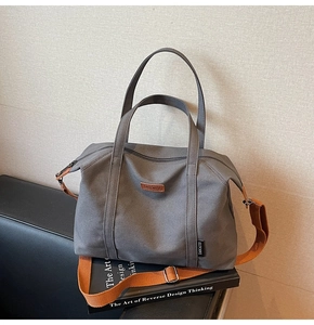 Detail of grey canvas tote bag with orange strap on a book over a black leather sofa