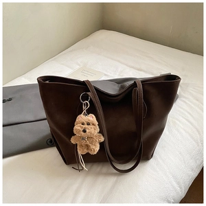 Deep brown faux leather tote bag with cute plush puppy pendant on a white bedding background