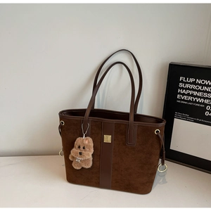 Close-up of brown suede tote bag featuring golden buckle and cute plush puppy keychain