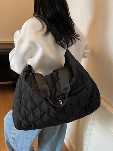 Large black quilted tote bag with floral embroidery and adjustable strap on a model