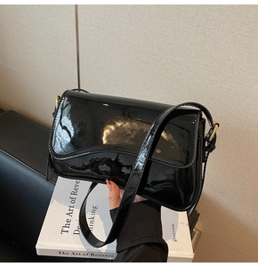 Detail of high-gloss black patent leather shoulder bag with golden metal buckle hardware