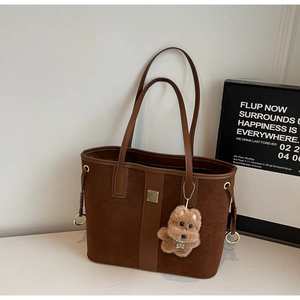 Close-up of brown suede tote bag with metal buckle and plush bear pendant detail
