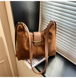 Detail of soft brown suede tote bag featuring a golden curved metal accent and leather strap