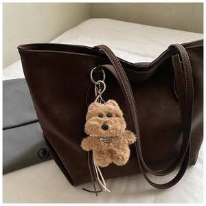 Close-up of light brown plush dog charm with pearl chain on a brown tote bag